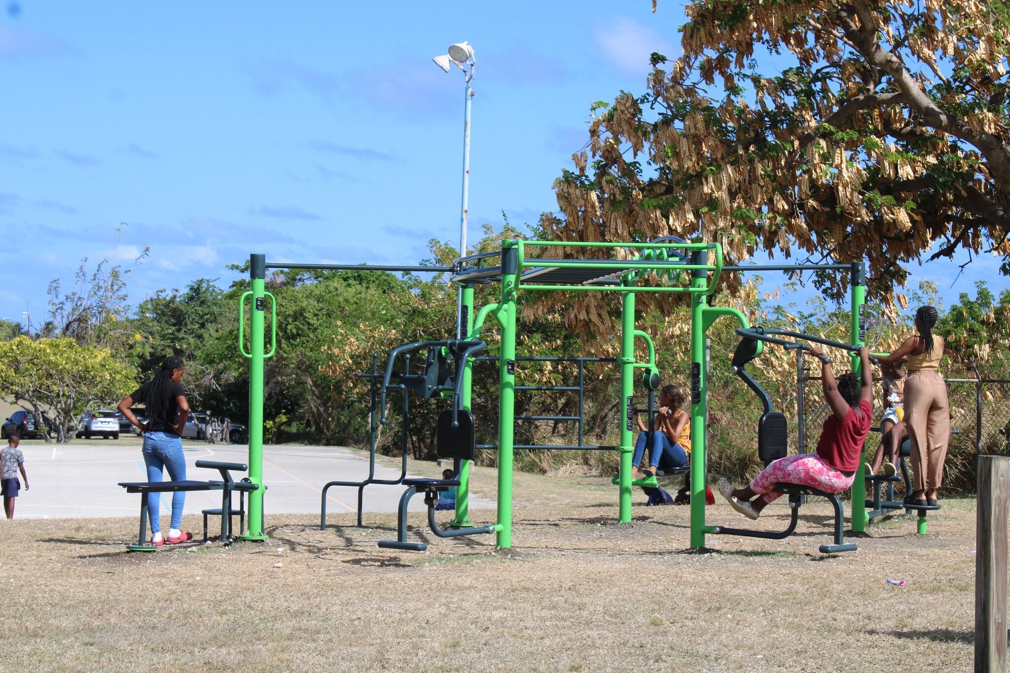 Wide view of a green multi-station outdoor gym with community members using the equipment