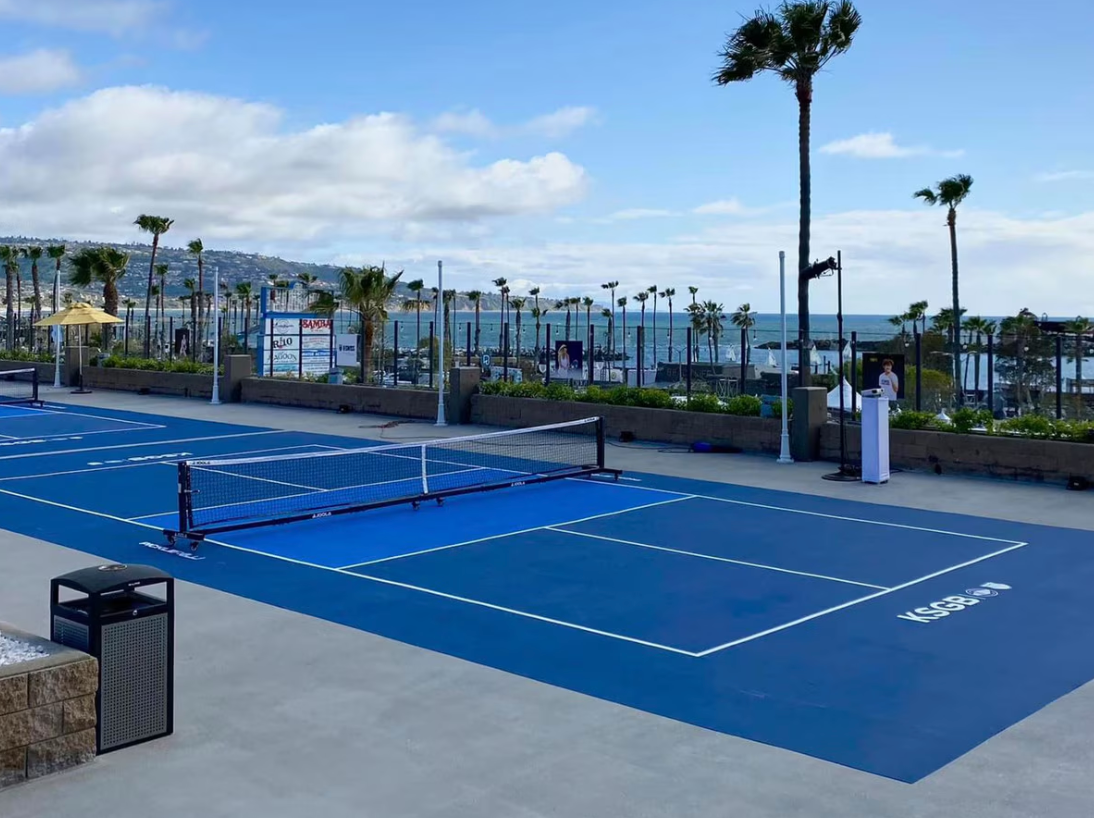 Blue outdoor pickleball courts overlooking the sea, surrounded by palm trees